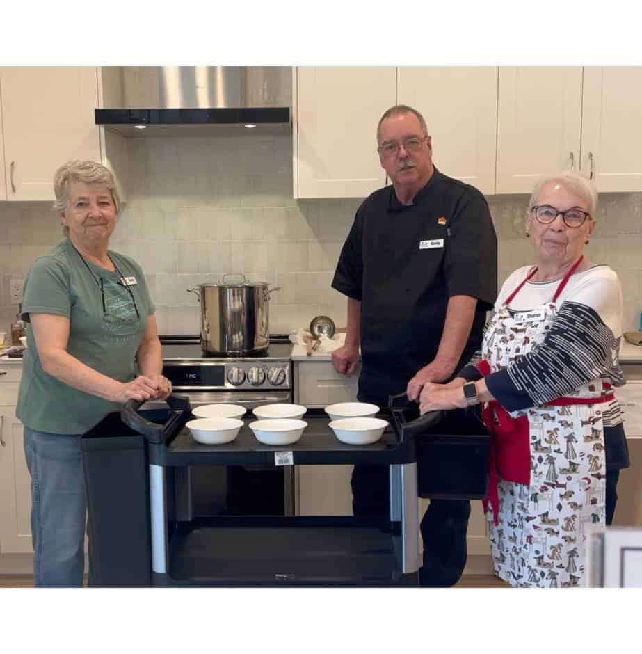 Three people serving food in community kitchen.